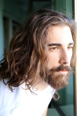 Uzun saçlı ve sakallı şık, beyaz bir adam balkonda poz veriyor. Tarz, trendler, moda konsepti.