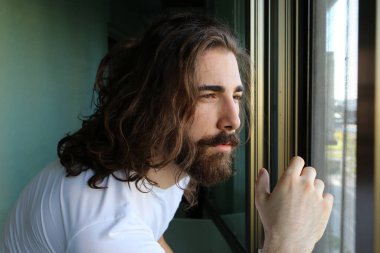 Uzun saçlı ve sakallı şık, beyaz bir adam balkonda poz veriyor. Tarz, trendler, moda konsepti.