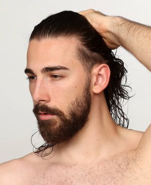 Uzun saçlı ve sakallı çekici erkek model izole bir arka planda stüdyoda poz veriyor. Tarz, trendler, moda konsepti.
