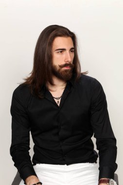 Genç, modaya uygun, uzun saçlı ve sakallı bir erkek model izole edilmiş arka planda stüdyoda poz veriyor. Moda, iş, modellik konsepti.