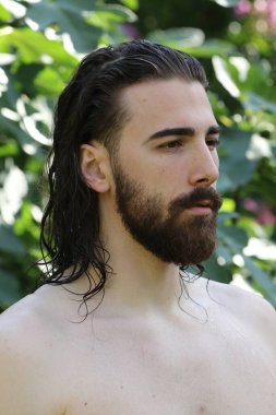 Genç, çekici erkek model, uzun saçlı ve sakallı, doğada poz veren. Tarz, trendler, moda konsepti.