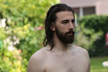 Genç, çekici erkek model, uzun saçlı ve sakallı, doğada poz veren. Tarz, trendler, moda konsepti.