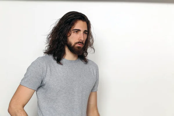 Attractive male model with long hair and beard posing in studio on isolated background. Style, trends, fashion concept.