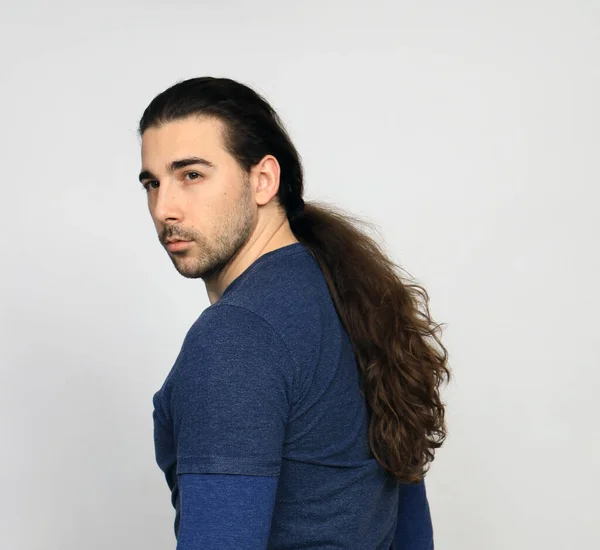 Attractive male model with long hair and beard is posing in studio. Style, trends, fashion concept.