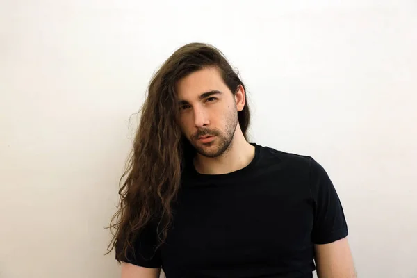 Attractive male model with long hair and beard is posing in studio. Style, trends, fashion concept.