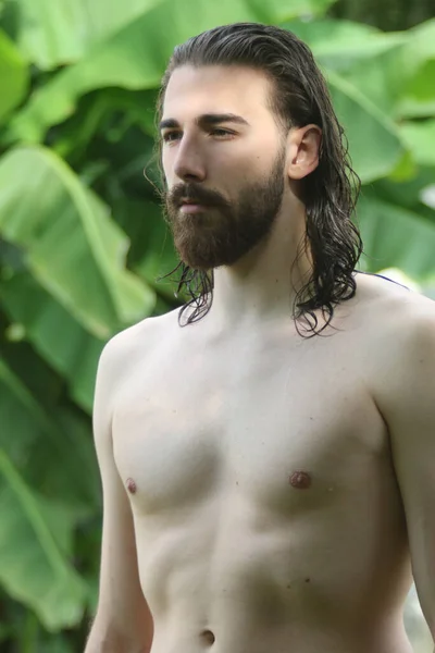 Young, attractive male model with long hair and beard posing in nature. Style, trends, fashion concept.