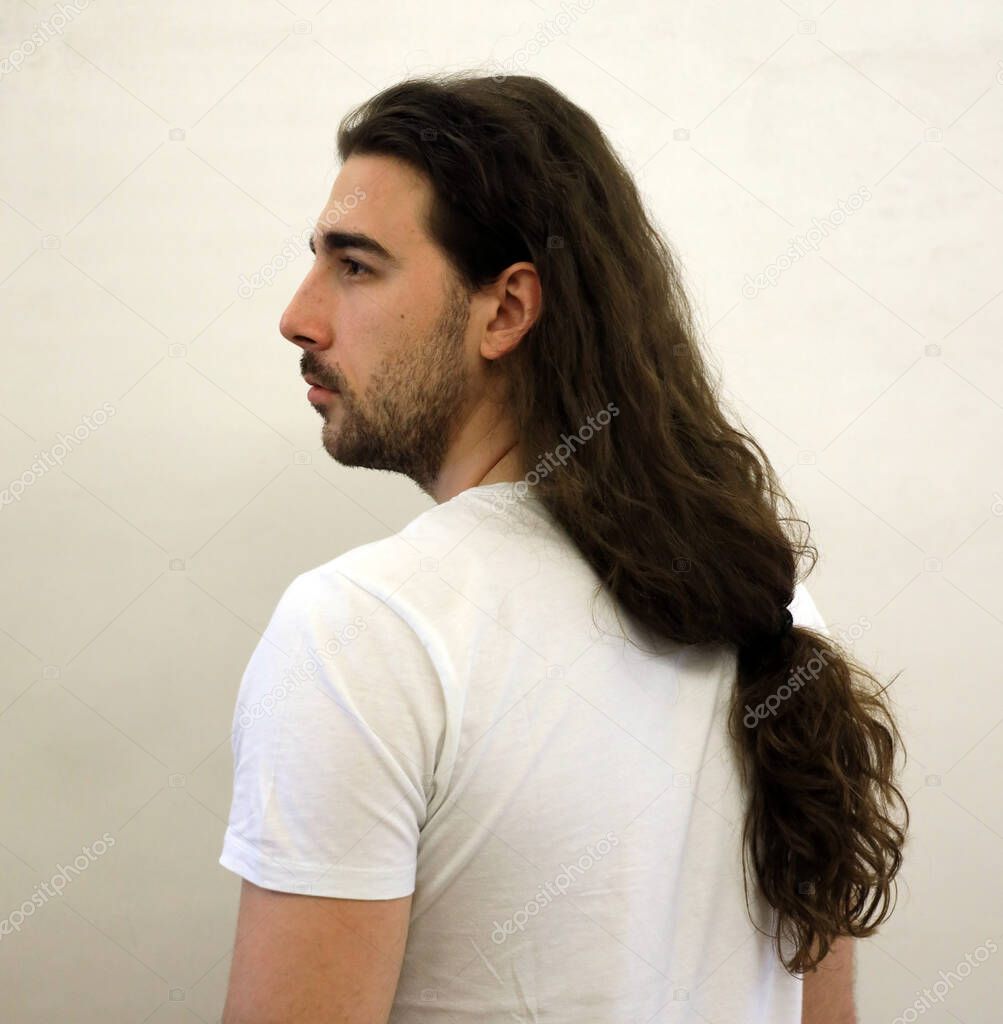 Attractive male model with long hair and beard is posing in studio. Style, trends, fashion concept.