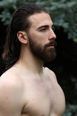 Genç, çekici erkek model, uzun saçlı ve sakallı, doğada poz veren. Tarz, trendler, moda konsepti.