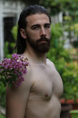 Genç, çekici erkek model, uzun saçlı ve sakallı, doğada poz veren. Tarz, trendler, moda konsepti.