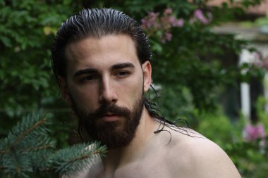Genç, çekici erkek model, uzun saçlı ve sakallı, doğada poz veren. Tarz, trendler, moda konsepti.
