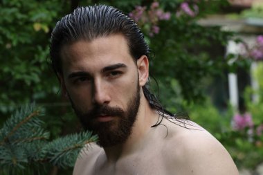 Genç, çekici erkek model, uzun saçlı ve sakallı, doğada poz veren. Tarz, trendler, moda konsepti.