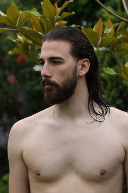 Genç, çekici erkek model, uzun saçlı ve sakallı, doğada poz veren. Tarz, trendler, moda konsepti.