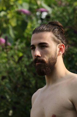 Genç, çekici erkek model, uzun saçlı ve sakallı, doğada poz veren. Tarz, trendler, moda konsepti.