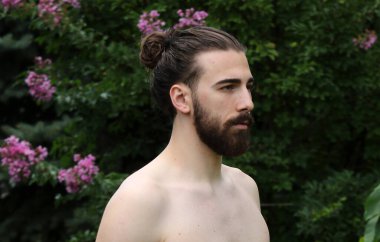 Genç, çekici erkek model, uzun saçlı ve sakallı, doğada poz veren. Tarz, trendler, moda konsepti.