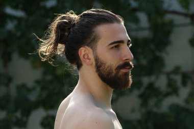 Genç, çekici erkek model, uzun saçlı ve sakallı, doğada poz veren. Tarz, trendler, moda konsepti.