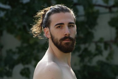 Genç, çekici erkek model, uzun saçlı ve sakallı, doğada poz veren. Tarz, trendler, moda konsepti.