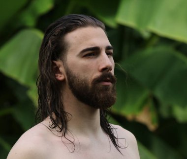 Genç, çekici erkek model, uzun saçlı ve sakallı, doğada poz veren. Tarz, trendler, moda konsepti.