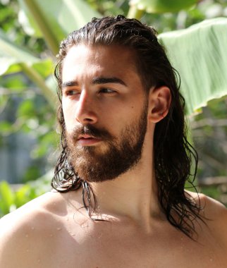 Genç, çekici erkek model, uzun saçlı ve sakallı, doğada poz veren. Tarz, trendler, moda konsepti.