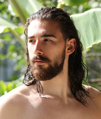 Genç, çekici erkek model, uzun saçlı ve sakallı, doğada poz veren. Tarz, trendler, moda konsepti.