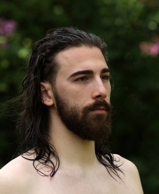 Genç, çekici erkek model, uzun saçlı ve sakallı, doğada poz veren. Tarz, trendler, moda konsepti.