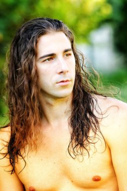 Çok uzun saçlı çekici bir adam vahşi doğada poz veriyor. Modelleme ve Moda Konsepti.