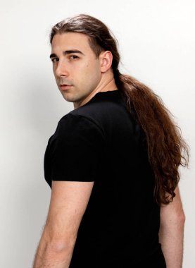 Uzun kıvırcık saçlı çekici genç adam stüdyoda poz veriyor. Tarz, trendler, moda konsepti.