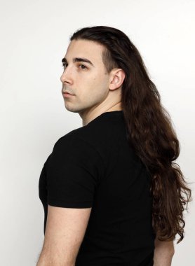 Uzun kıvırcık saçlı çekici genç adam stüdyoda poz veriyor. Tarz, trendler, moda konsepti.