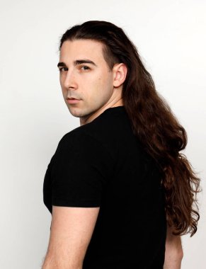 Uzun kıvırcık saçlı çekici genç adam stüdyoda poz veriyor. Tarz, trendler, moda konsepti.