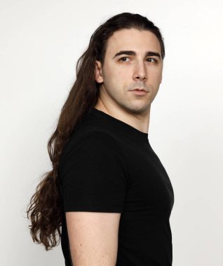 Uzun kıvırcık saçlı çekici genç adam stüdyoda poz veriyor. Tarz, trendler, moda konsepti.