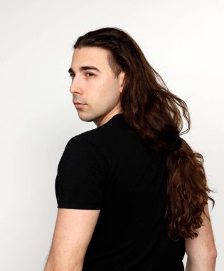 Uzun kıvırcık saçlı çekici genç adam stüdyoda poz veriyor. Tarz, trendler, moda konsepti.