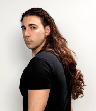 Uzun kıvırcık saçlı çekici genç adam stüdyoda poz veriyor. Tarz, trendler, moda konsepti.