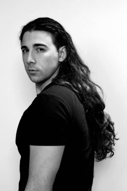 Uzun kıvırcık saçlı çekici genç adam stüdyoda poz veriyor. Tarz, trendler, moda konsepti.