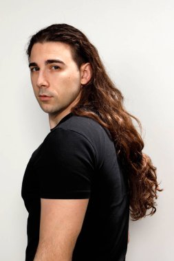 Uzun kıvırcık saçlı çekici genç adam stüdyoda poz veriyor. Tarz, trendler, moda konsepti.