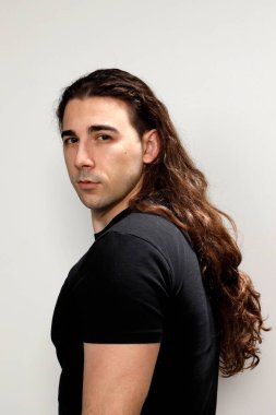 Uzun kıvırcık saçlı çekici genç adam stüdyoda poz veriyor. Tarz, trendler, moda konsepti.