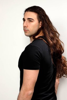 Uzun kıvırcık saçlı çekici genç adam stüdyoda poz veriyor. Tarz, trendler, moda konsepti.