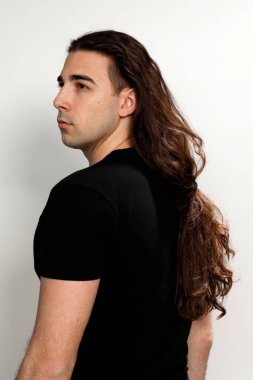 Uzun kıvırcık saçlı çekici genç adam stüdyoda poz veriyor. Tarz, trendler, moda konsepti.