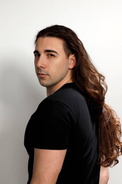 Uzun kıvırcık saçlı çekici genç adam stüdyoda poz veriyor. Tarz, trendler, moda konsepti.