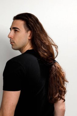 Uzun kıvırcık saçlı çekici genç adam stüdyoda poz veriyor. Tarz, trendler, moda konsepti.