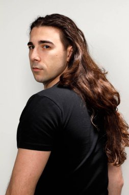 Uzun kıvırcık saçlı çekici genç adam stüdyoda poz veriyor. Tarz, trendler, moda konsepti.