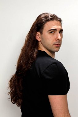 Uzun kıvırcık saçlı çekici genç adam stüdyoda poz veriyor. Tarz, trendler, moda konsepti.