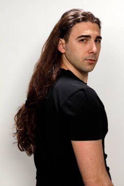 Uzun kıvırcık saçlı çekici genç adam stüdyoda poz veriyor. Tarz, trendler, moda konsepti.