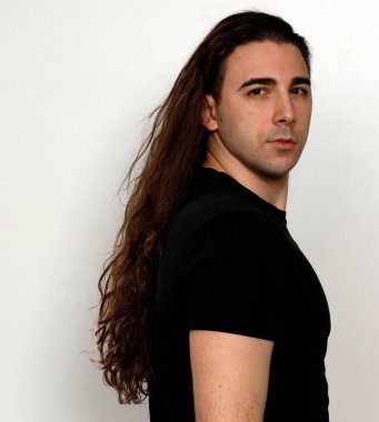 Uzun kıvırcık saçlı çekici genç adam stüdyoda poz veriyor. Tarz, trendler, moda konsepti.