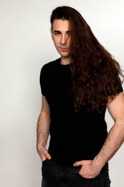 Uzun kıvırcık saçlı çekici genç adam stüdyoda poz veriyor. Tarz, trendler, moda konsepti.