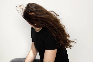 Uzun kıvırcık saçlı çekici genç adam stüdyoda poz veriyor. Tarz, trendler, moda konsepti.