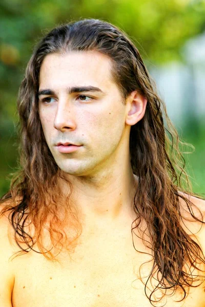 Attractive guy with very long hair is posing in the wild. Modeling and Fashion Concept.