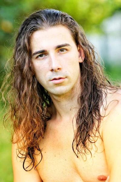 Attractive guy with very long hair is posing in the wild. Modeling and Fashion Concept.