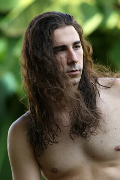 Attractive guy with very long hair is posing in the wild. Modeling and Fashion Concept.