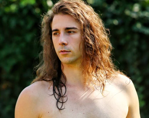 Attractive guy with very long hair is posing in the wild. Modeling and Fashion Concept.