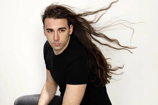 Attractive young guy with very long curly hair is posing in studio. Style, trends, fashion concept.