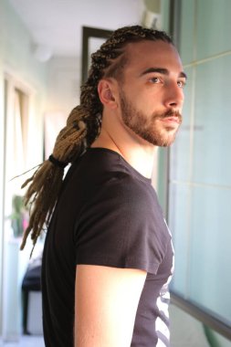 Attractive, young blonde bearded male model with combination of braids and dreadlocks posing on the balcony. Style, trends, fashion concept clipart
